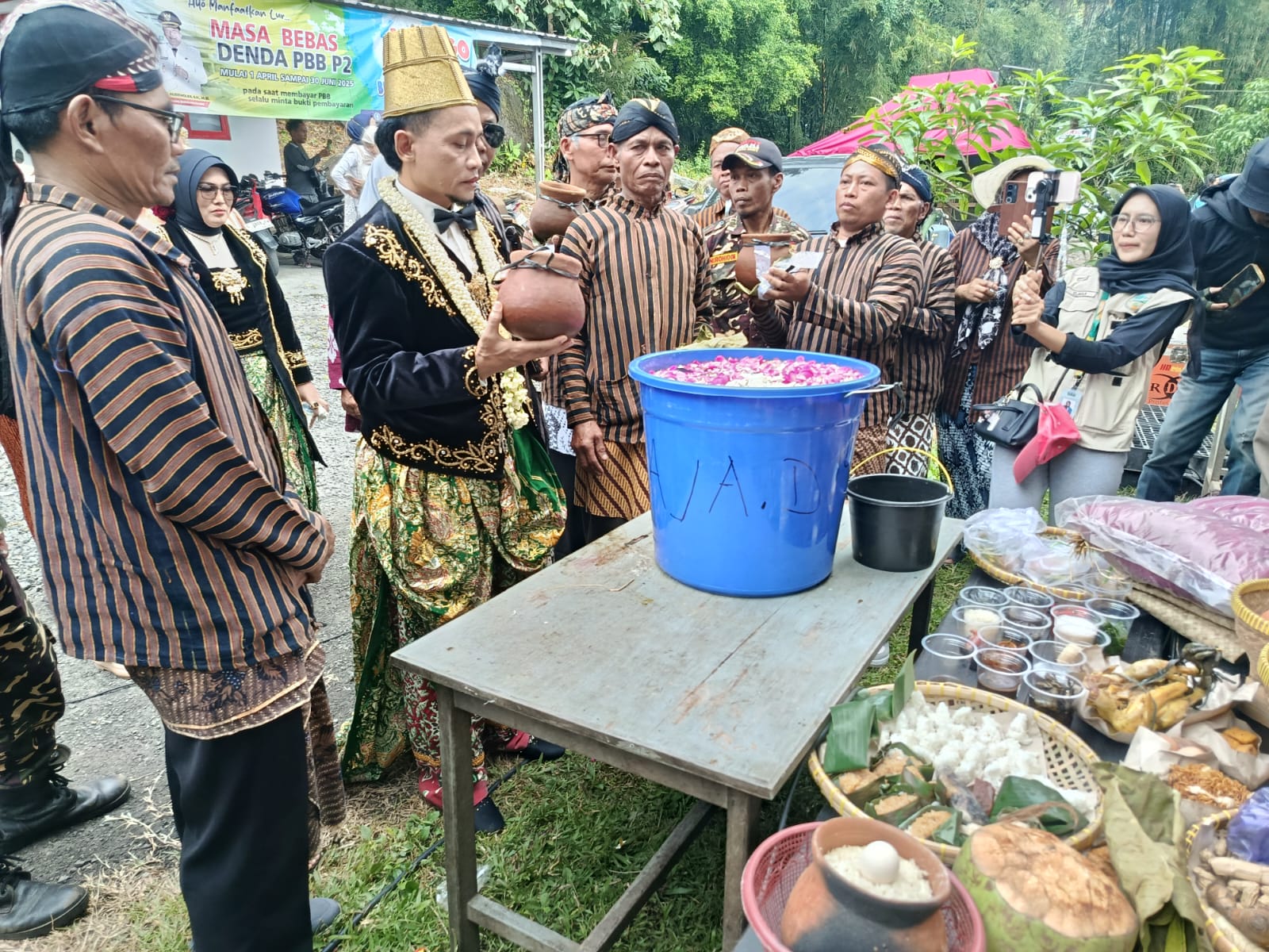 Kepala Desa Beluk (Rinto) berdiri di tengah mengenakan busana adat Jawa sambil memegang kendi